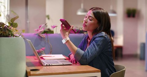 African american woman working in coworking lounge using smartphone and laptop with plants