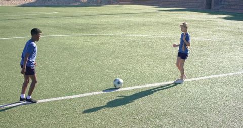 Diverse youth soccer players practicing passing drill on sunny turf field showing teamwork