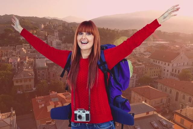 Vibrant image of a joyful woman with outstretched arms, camera around neck, and backpack, set against a backdrop of city buildings at sunset or sunrise. Ideal for travel blogs, tourism advertisements, adventure magazines, or promotional materials for tourist destinations.