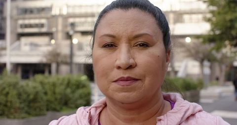 Mature woman standing in urban plaza wearing pink hoodie and nose stud, calm portrait