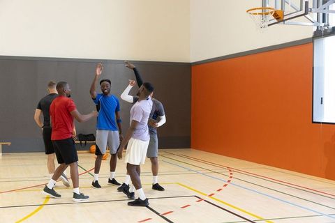 Diverse male teammates celebrating on indoor basketball court after pickup game, teamwork