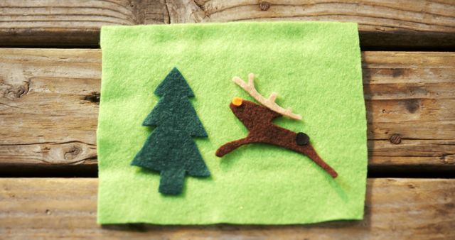 A green felt fabric features a simple Christmas-themed craft with a tree and reindeer cutouts, with copy space. These handmade decorations evoke a cozy, festive atmosphere ideal for the holiday season.