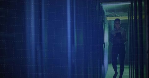 Technology specialist checking tablet in dimly lit datacenter corridor