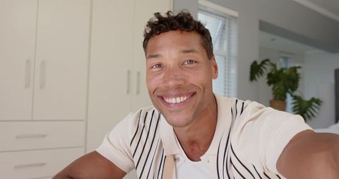 Mid-adult man smiling and holding smartphone in sunlit bedroom for lifestyle content