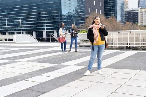 Senior woman speaking into smartphone in city plaza demonstrating voice assistant use