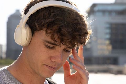 Young man listening to music with white over-ear headphones in sunlit urban background