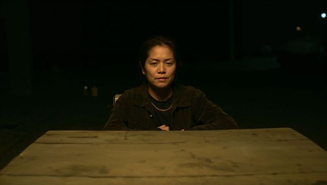 Moody night portrait of asian woman sitting at stained table under single spotlight