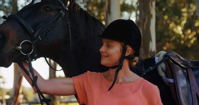 A middle-aged Caucasian woman wearing a riding helmet stands close to a horse, with copy space. Her affectionate pose with the animal suggests a bond and love for equestrian activities.