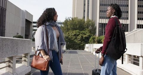 Diverse coworkers chatting on urban campus bridge with suitcase and leather handbag