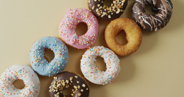 Variety of colorful donuts with different toppings positioned on neutral background. Includes donuts with sprinkles, chocolate glaze, and nuts. Perfect for use in bakery advertising, dessert blogs, or culinary magazines.