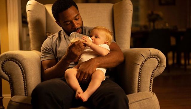 Evening bonding moment: black father bottle-feeding baby in cozy armchair, home parenting