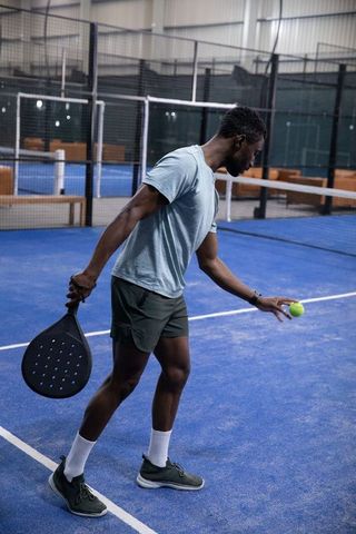 African american male serving on indoor blue padel court holding racket and yellow ball