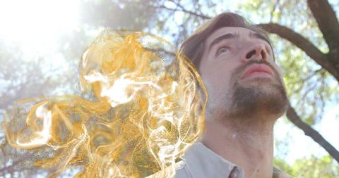 Contemplative man gazing upward in sunlit forest with swirling golden particle mist