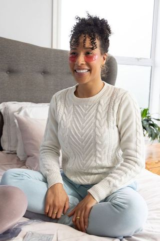 African american woman enjoying skincare routine with under-eye gel patches on bed morning