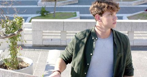 Young man leaning on concrete balustrade on urban terrace looking into distance