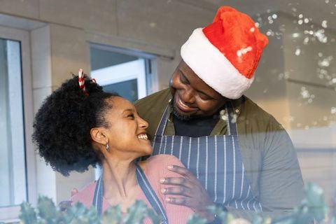 African American couple sharing warm holiday hug while baking in cozy kitchen, wearing Santa hat