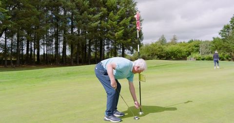 Senior Man Retrieving Golf Ball While Putting Outdoors