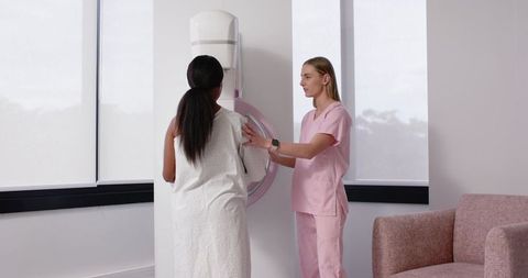 Female nurse positioning patient for mammogram screening in minimalist clinic room