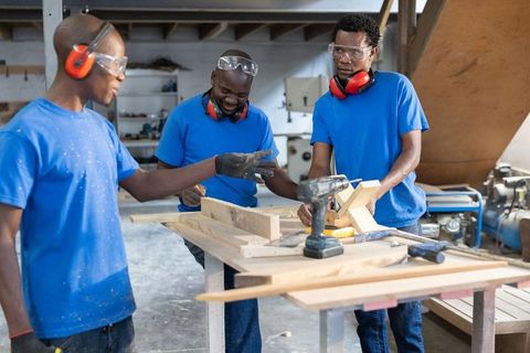 Male woodworkers collaborating on assembly of handcrafted timber furniture in workshop