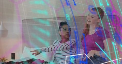 Two women chatting on bed with neon holographic overlay relaxing and laughing in bedroom