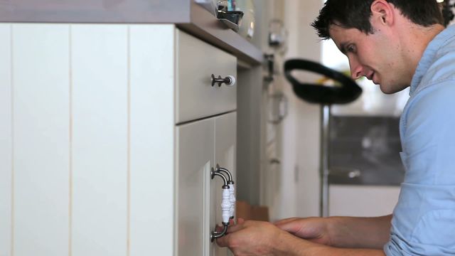 Man repairing kitchen cabinet using screwdriver, focusing on fixing handle. Useful for illustrating home improvement, DIY projects, renovation services, and maintenance tutorials.