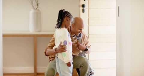 Father kneeling and hugging african american daughter in sunlit entryway, warm homecoming