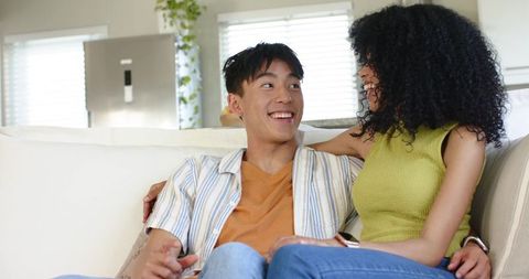 Smiling interracial couple relaxing on cozy sofa holding smartphone in bright modern home