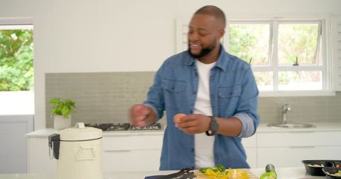 African american man preparing vegetables while holding egg on modern kitchen countertop