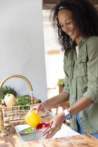 African american woman washing bell peppers at kitchen sink, healthy cooking lifestyle