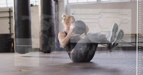 Woman performing v-sit with medicine ball in industrial gym core strength workout