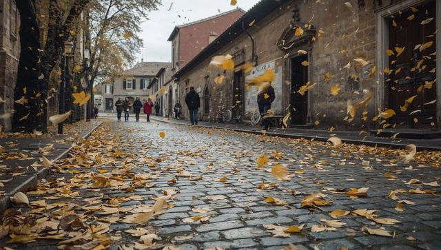 Autumn leaves swirling over wet cobblestone street while pedestrians walk past shops
