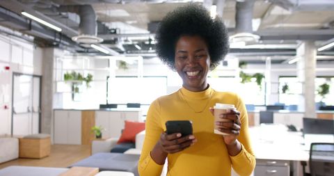 Happy Businesswoman Using Smartphone and Holding Coffee in Modern Office