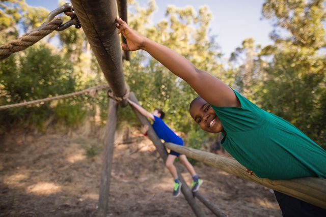 Boy smiling while participating in an outdoor obstacle course during a boot camp. Ideal for use in advertisements for children's fitness programs, summer camps, outdoor adventure activities, and educational materials promoting physical activity and teamwork.