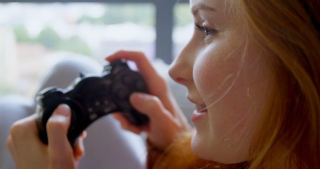 Young Caucasian woman plays video games at home, with copy space. She's focused on the screen, enjoying her leisure time with a gaming controller in hand.