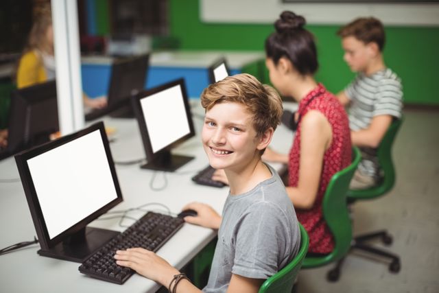 Schoolboy smiling while studying in a computer classroom with classmates. Ideal for educational content, technology in education, school brochures, and digital learning resources.