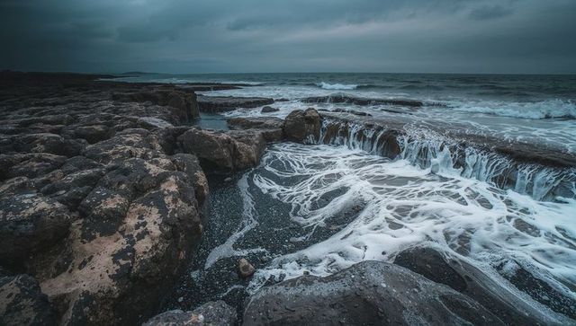 Rugged coastline cascading sea foam over flat rock ledges under moody storm sky