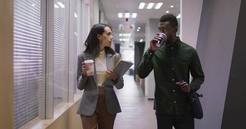 Colleagues walking and conversing in office corridor with coffee