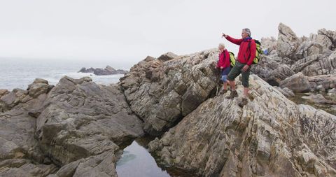 Senior hikers exploring rocky seashore with backpacks