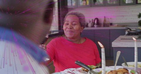Smiling mature woman toasting with wine at cozy candlelit kitchen table for family celebration