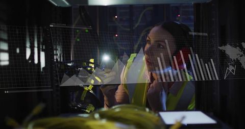 Female technician inspecting server rack in hi-vis vest holding torch with yellow network cables