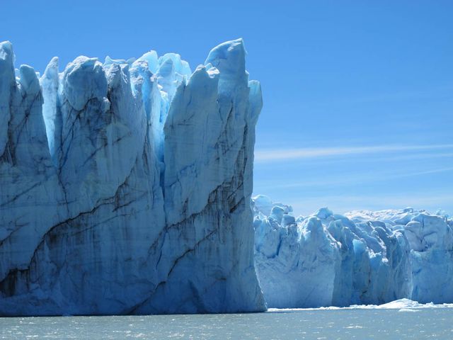 View of towering ice walls of Perito Moreno Glacier standing against a clear blue sky. Located in Argentina's Patagonia region, this glacier is known for its stability compared to others in the area. This photo is ideal for travel blogs, environmental awareness campaigns, nature documentaries, and educational materials about glaciers and their impact on sea level rise.