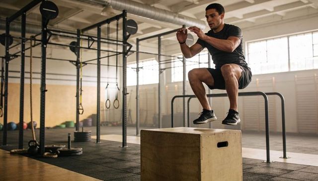 Fit athlete performing explosive plyometric box jump in industrial crossfit gym strength
