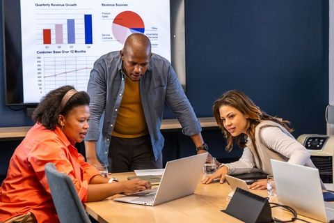 Diverse team collaborating and analyzing charts on laptops in modern conference room