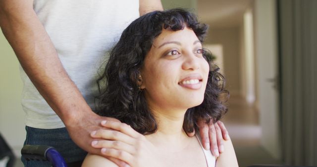 Image shows a woman in a wheelchair smiling while a supportive companion stands behind her, providing assurance by holding her shoulders. This scene embodies concepts of caregiving, support, and positive disability inclusion. Ideal for use in healthcare, caregiving, disability advocacy, and inclusive community services.
