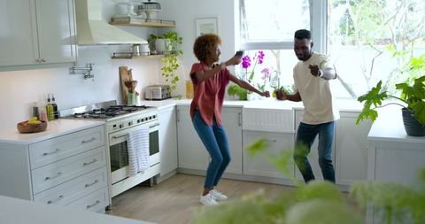 Sunlit modern kitchen couple dancing and laughing, holding smartphone, candid lifestyle