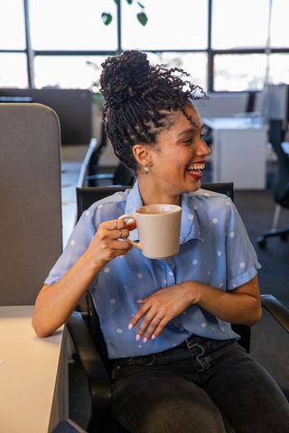 African american woman laughing holding ribbed ceramic coffee mug at modern office desk