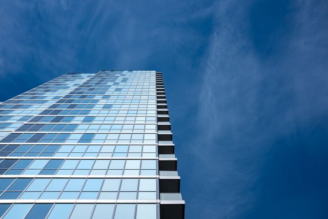 Tall glass skyscraper extending into the blue sky, conveying modern architecture and urban development. Could be used for corporate presentations, real estate advertisements, architectural portfolios, or city planning materials.