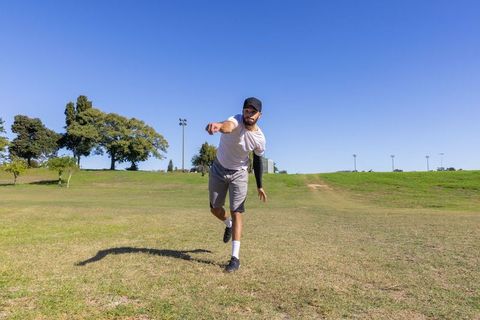 Athlete throwing disc on sunny park field wearing cap and compression sleeve