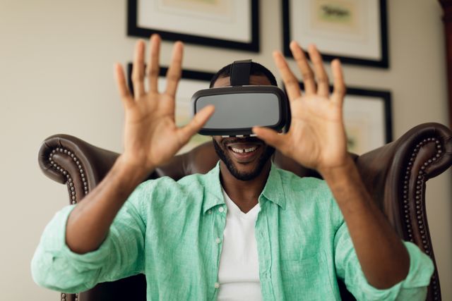 African-American man sitting on a leather chair, engaging with virtual reality using VR goggles. Ideal for technology-related content, virtual reality promotions, and modern lifestyle articles.