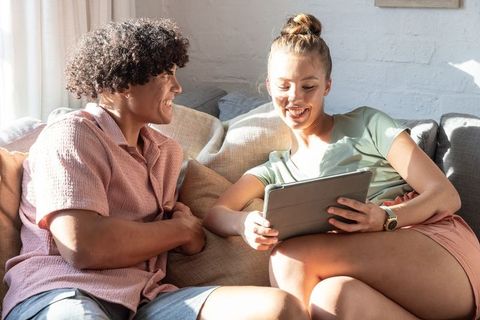 Young couple relaxing on sofa sharing tablet in sunlit cozy living room moment together